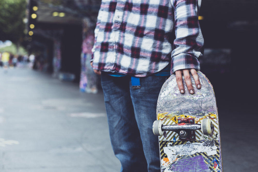 person with plaid shirt and jeans  holding a skateboard