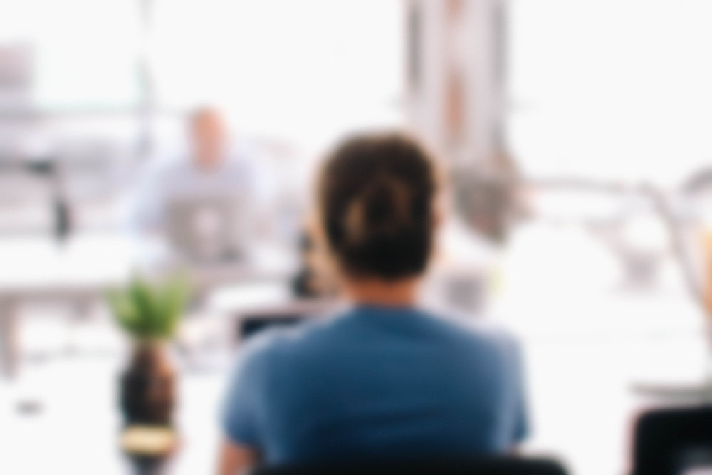 blurred image of person sitting at desk in front of laptop