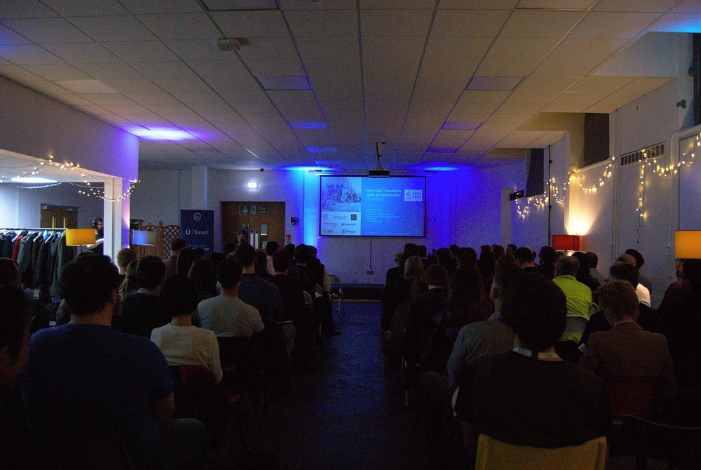 dimmed meeting room with delegates sitting theatre style watching presenter and screen